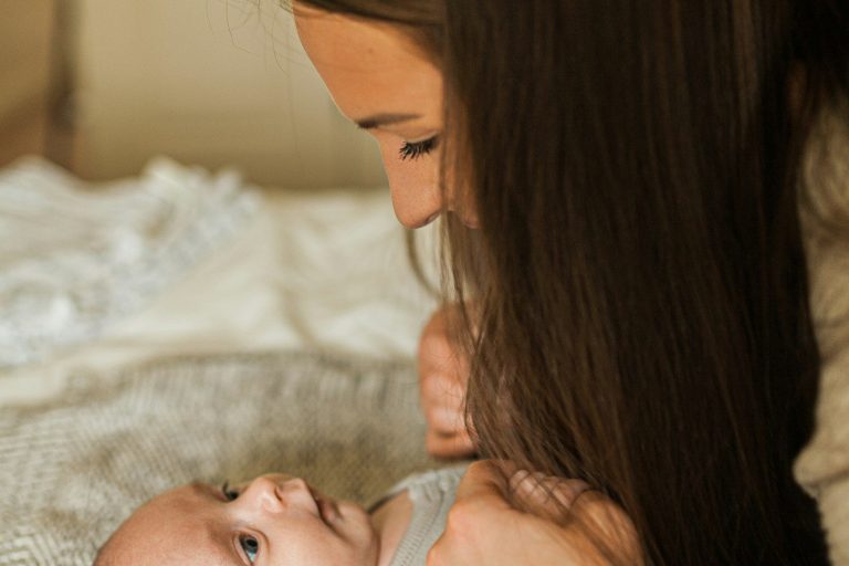 Eine Mutter schaut liebevoll auf ihr lächelndes Baby.