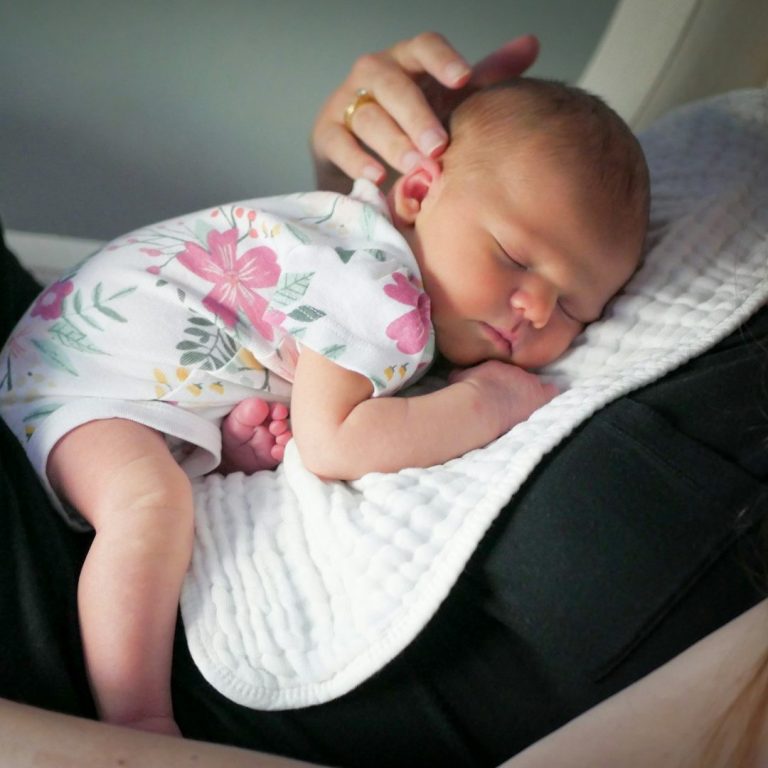Schlafberatung.jpg Neugeborenes Baby schläft in den Armen einer Person, eingekuschelt und friedlich.