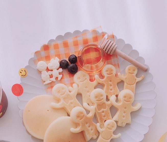 Beikostberatung.jpg Platte mit Keksfiguren, Honig, Beeren und Pfannkuchen auf einem karierten Tuch.
