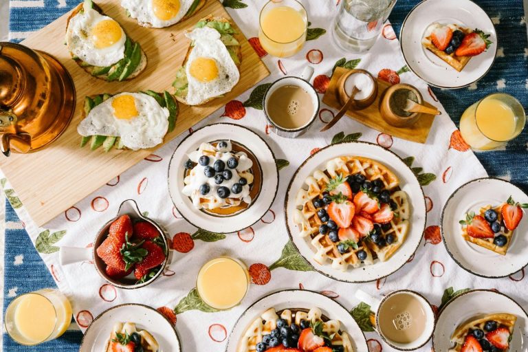 Frühstückstisch mit Waffeln, Beeren, Eiern, Saft und verschiedenen Snacks.